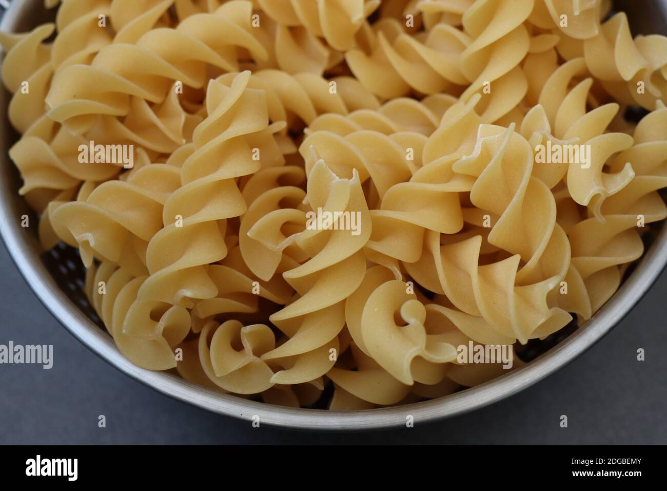Un primo piano della pasta fresca cruda di fusilli in un colander in acciaio su una superficie grigia Foto Stock