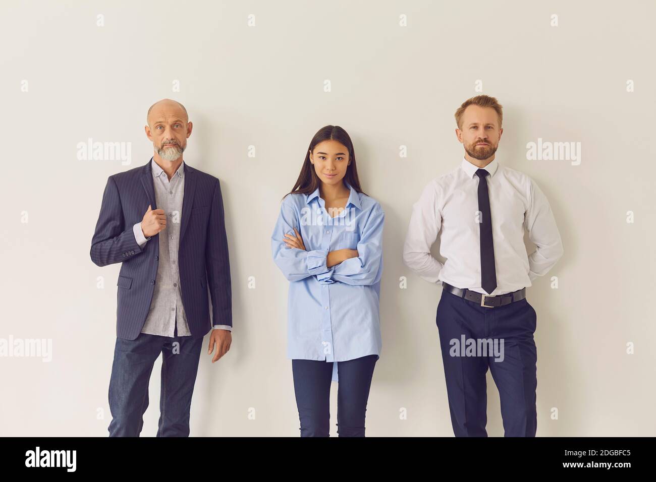 Dipendenti di uffici di diverse età ed etnie appoggiati contro il muro e guardando la fotocamera Foto Stock