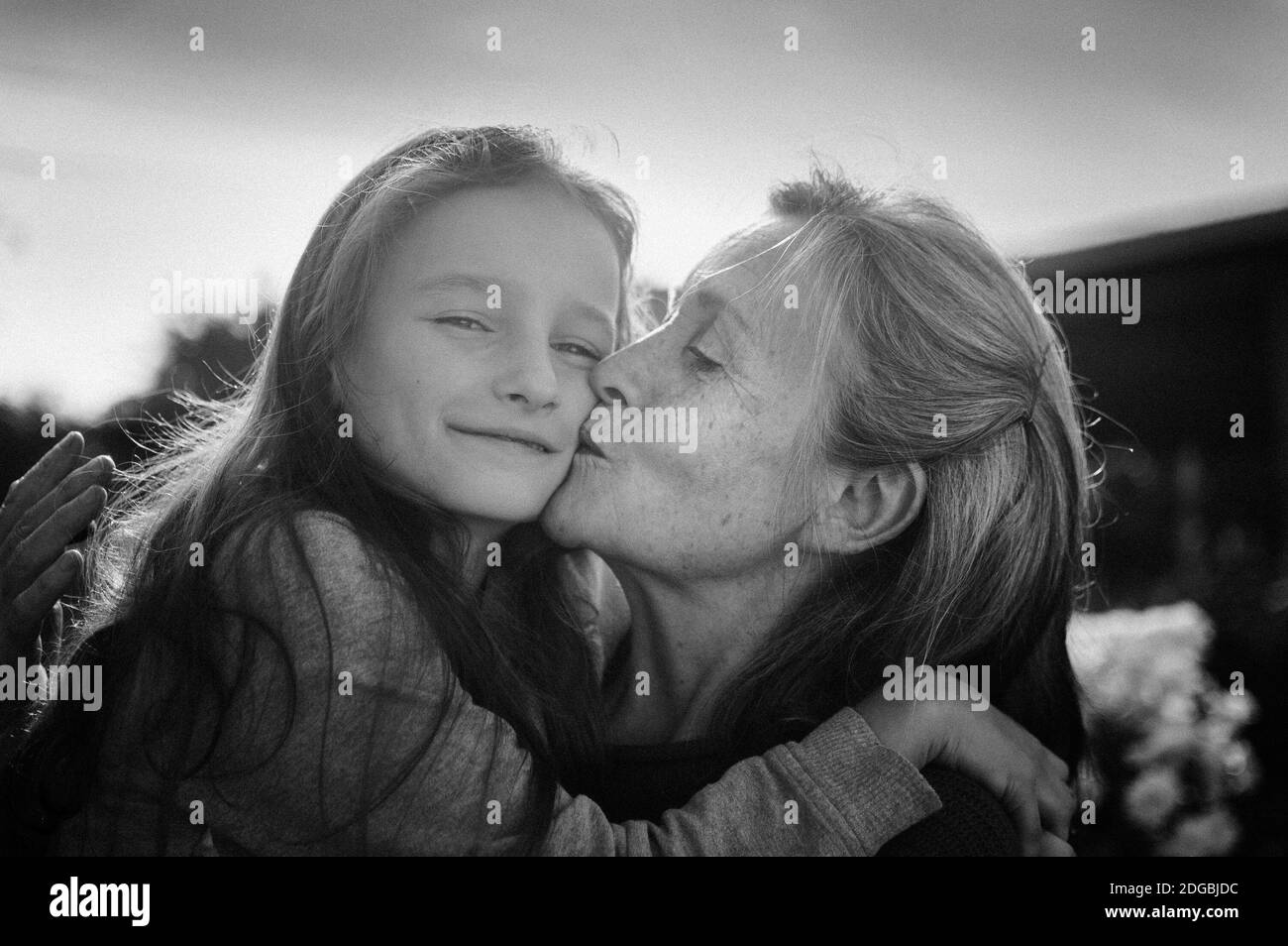 Ritratto in bianco e nero di nonna anziana con capelli grigi con la sua piccola nipote abbracciata in giardino e durante giornata di sole all'aperto Foto Stock