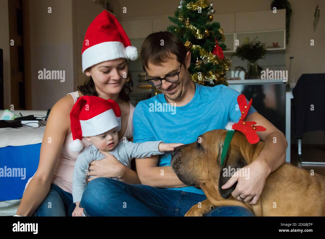 Ragazzo con la sindrome di Down con il suo cane e i genitori all'albero di Capodanno, foto di famiglia di Natale, famiglia con un bambino disabile Foto Stock