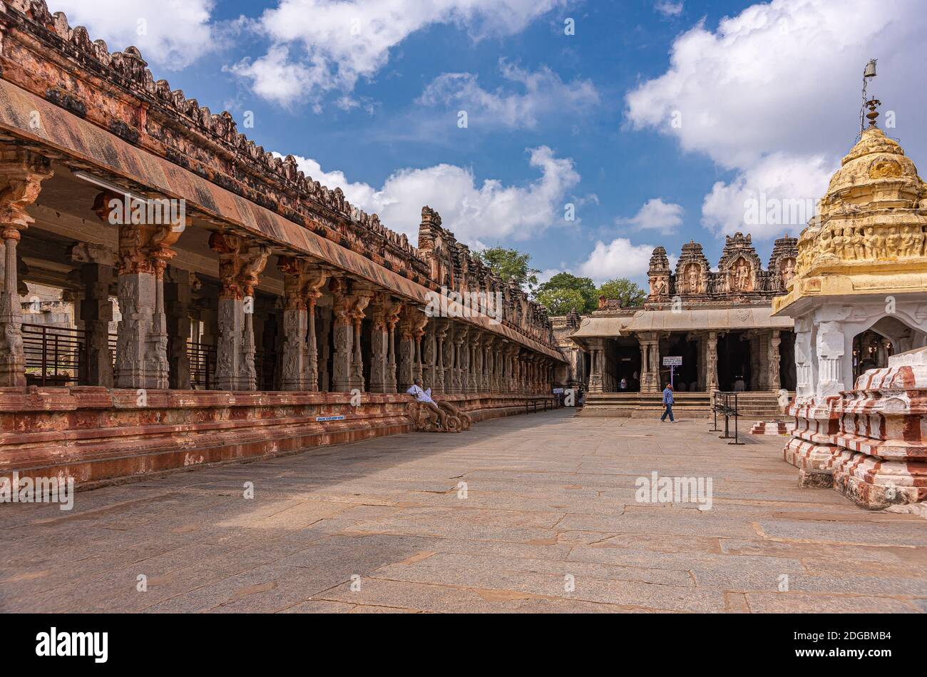 Hampi, Karnataka, India - 4 novembre 2013: Complesso del Tempio di Virupaksha. Sala arrugginita rossa a colonne sul lato con la parte superiore scolpita gialla su bianco santuario unde Foto Stock
