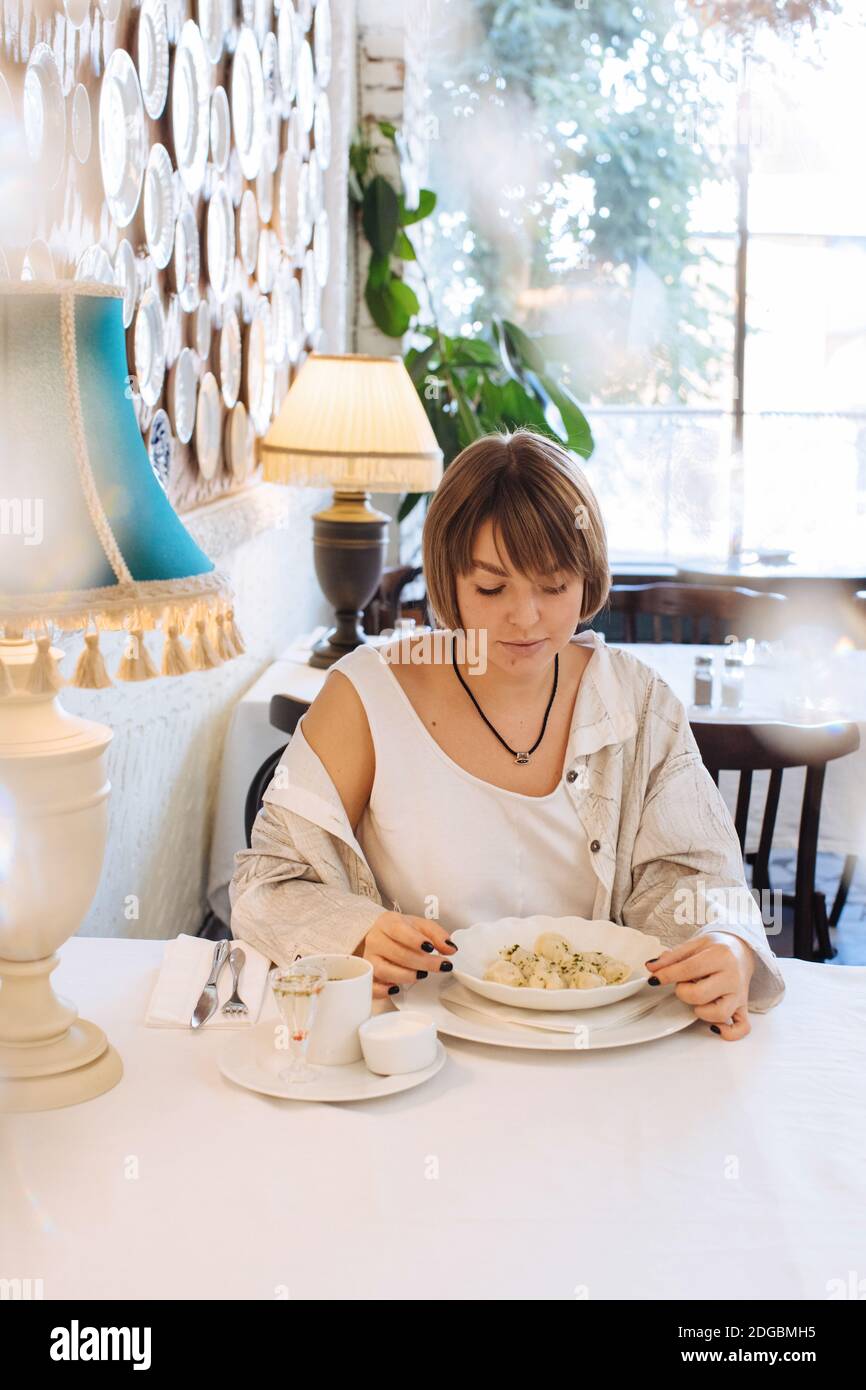 Donna seduta in un ristorante che mangia gnocchi pelmeni Foto Stock