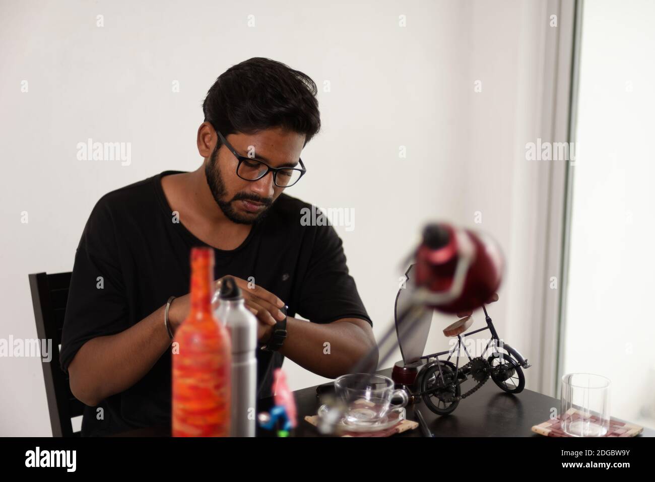 Un giovane indiano bengalese alto, scuro, bella bruna per la barba in una t-shirt casual è seduto su un tavolo da ufficio in un umore creativo. Foto Stock
