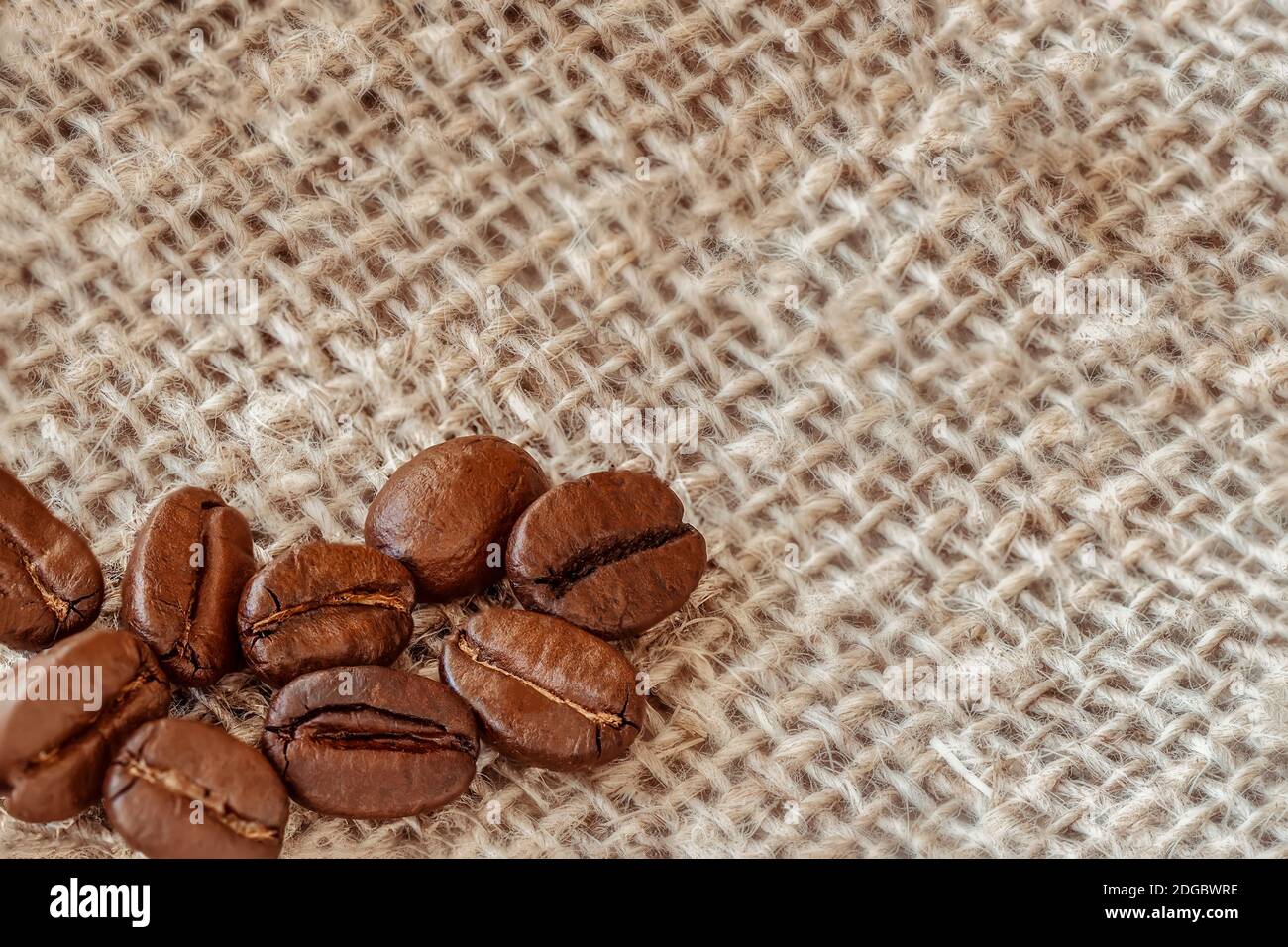 Primo piano di chicchi di caffè tostati aromatizzati sullo sfondo di sacco a frappè, spazio di copia, fuoco selettivo Foto Stock