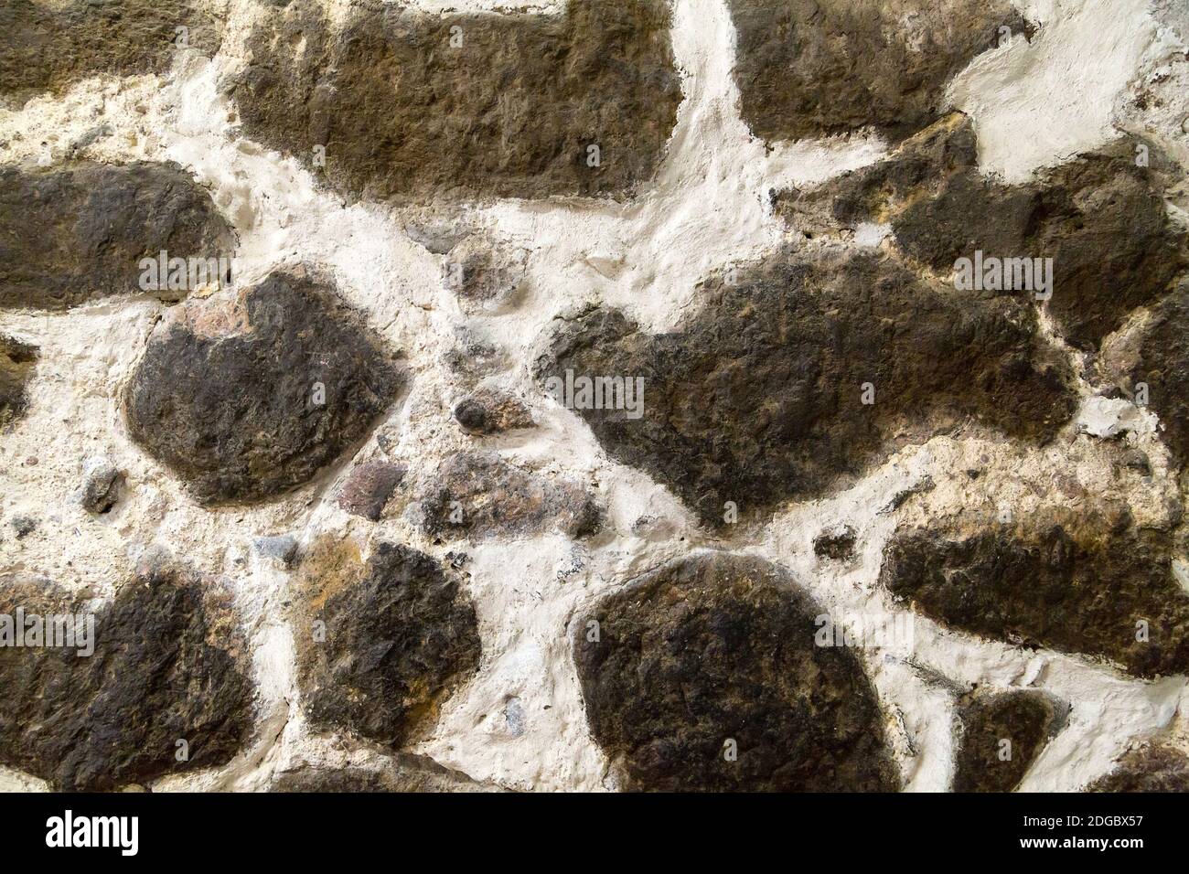 Pareti in pietra testurizzata costruite con grandi pietre grezze tenute insieme da grumi scuri di limesto di cemento bianco Foto Stock