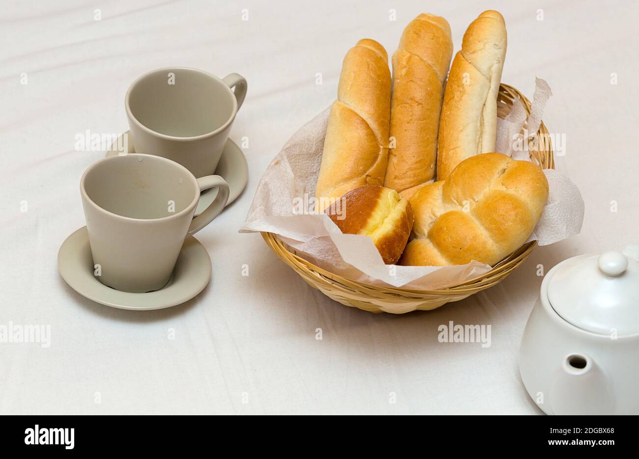 Colazione o pranzo presto due tazze una teiera con a. Cestino di pane fresco con baguette alla francese Foto Stock