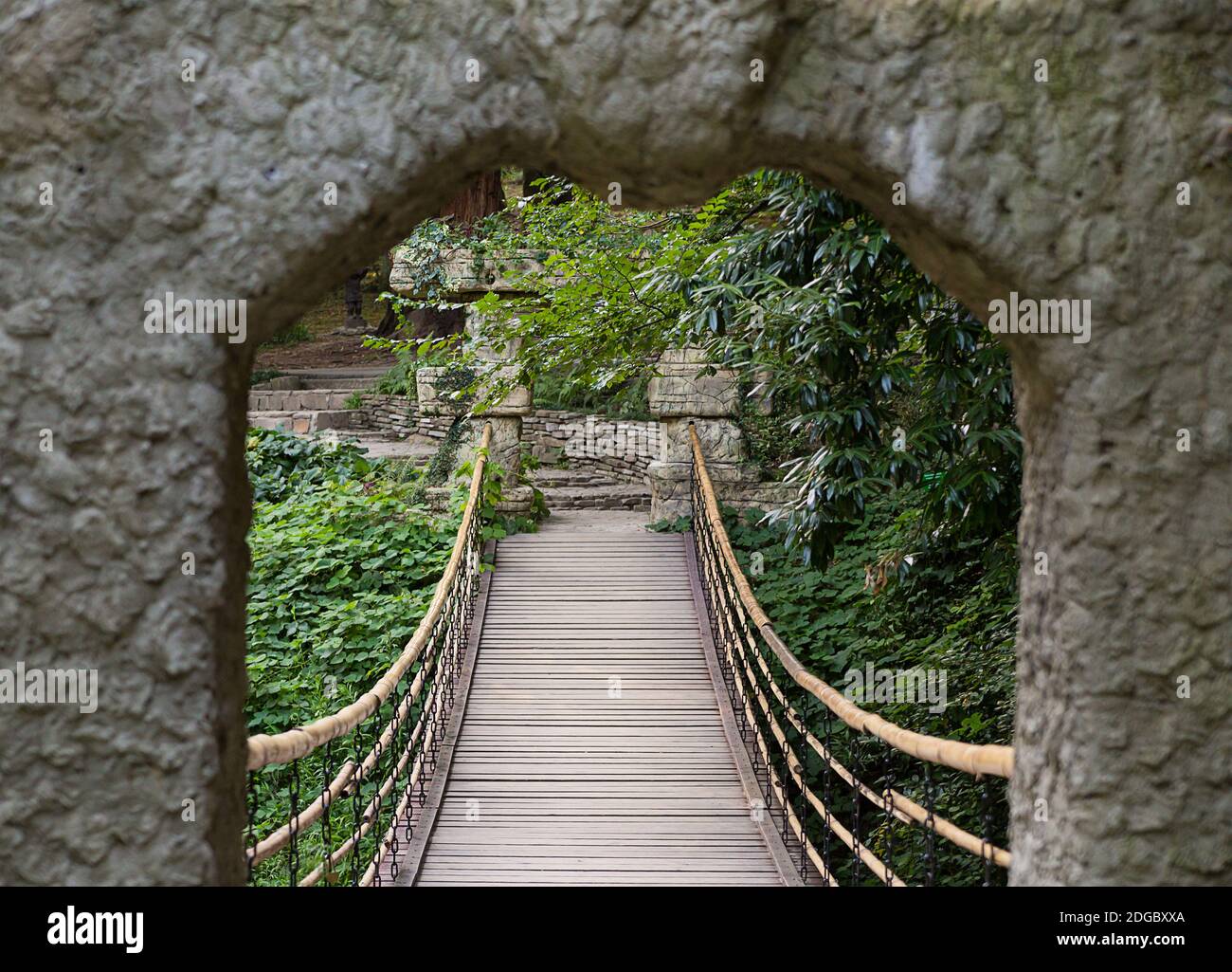 Passeggia attraverso il cancello ad arco del parco fino a una sospensione ponte di legno tra il verde Foto Stock