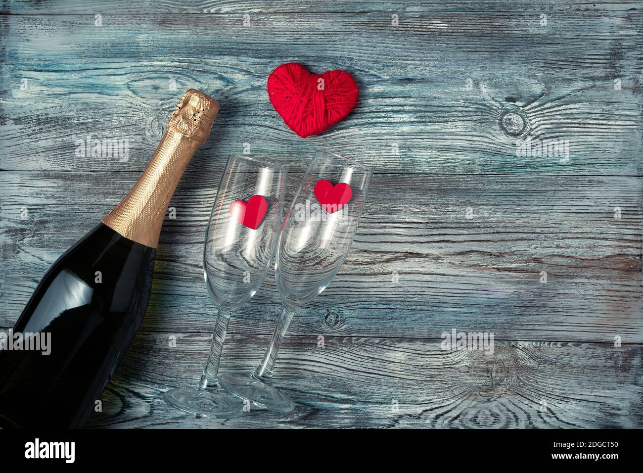 Champagne, due bicchieri e cuori rossi su sfondo di legno. Foto Stock