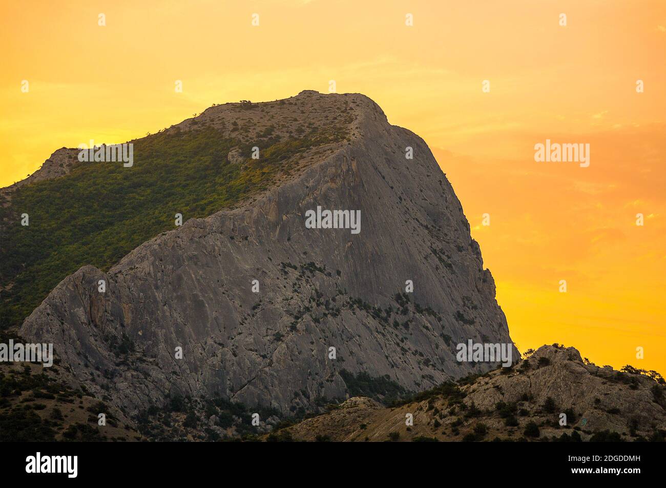Alta montagna grigia con un pendio pianeggiante coperto di verde in giallo arancio luce alba del sole Foto Stock