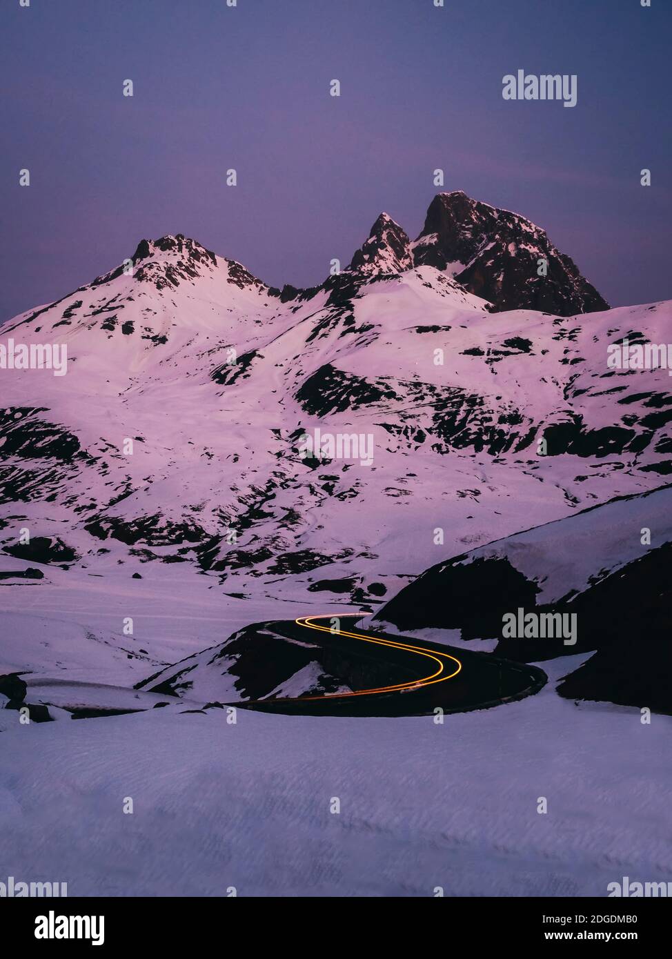 Auto sentieri luci su curve strada contro le montagne innevate durante l'alba al col du Pourtalet, Laruns, Francia Foto Stock