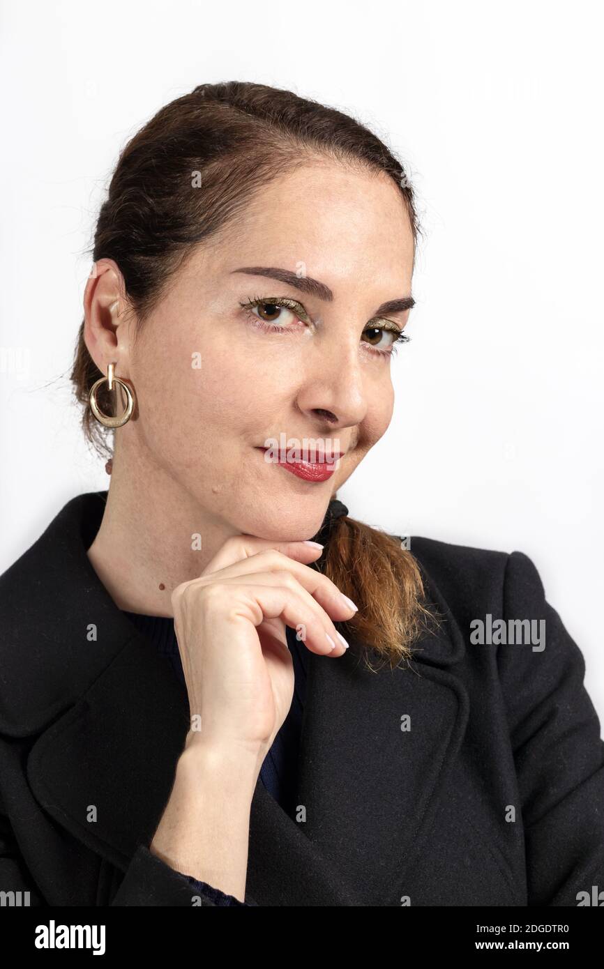 Bella donna con una mano sul mento fotocamera che indossa un cappotto, sorriso morbido Foto Stock