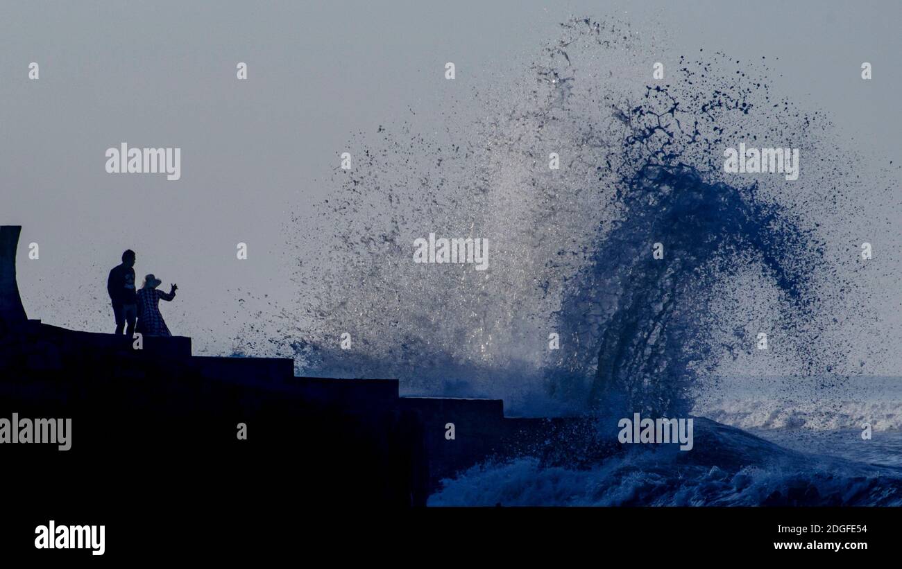Due persone che osservano le onde si schiantano contro gli interruttori sulla spiaggia di Cox's Bazar in Bangladesh. L'aumento del livello del mare e l'erosione della spiaggia hanno causato il crollo di demolitori ed edifici lungo la spiaggia. Foto Stock