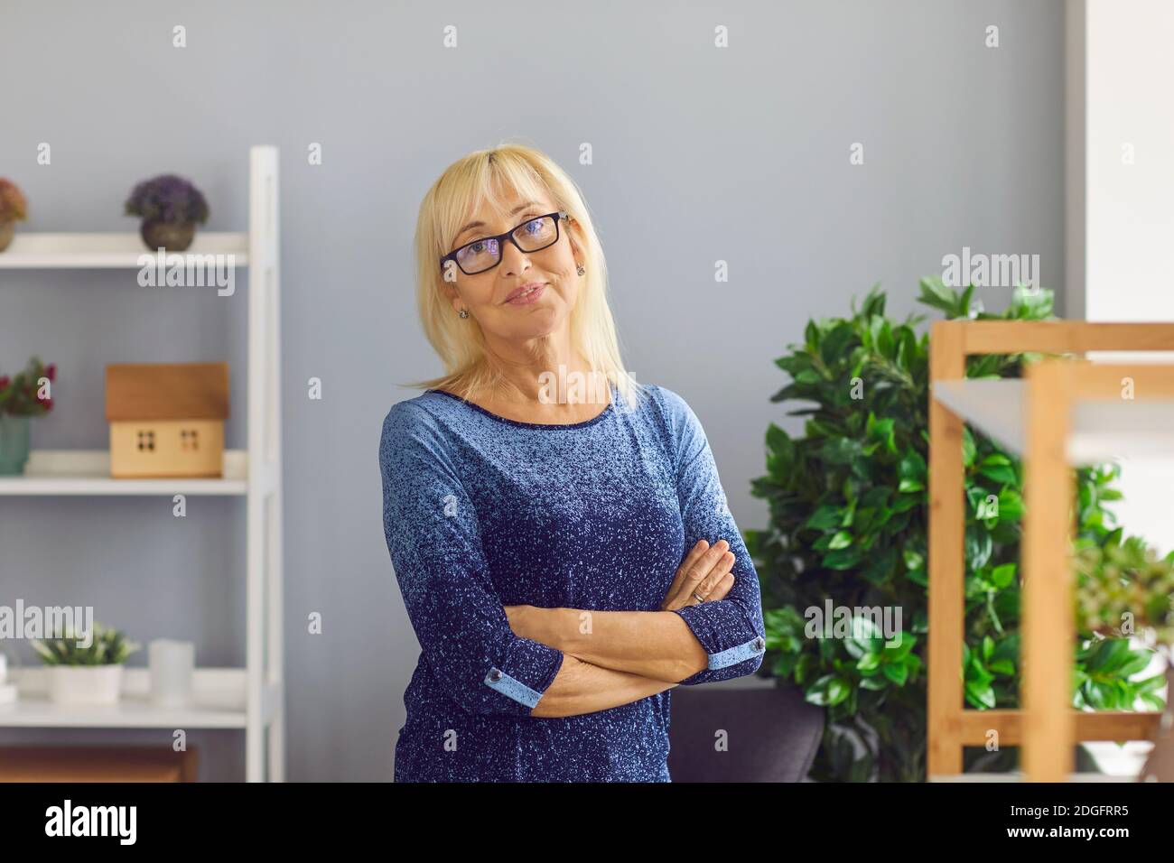 Ritratto di donna matura sorridente di mezza età con occhiali che guardano la macchina fotografica con le braccia incrociate. Foto Stock