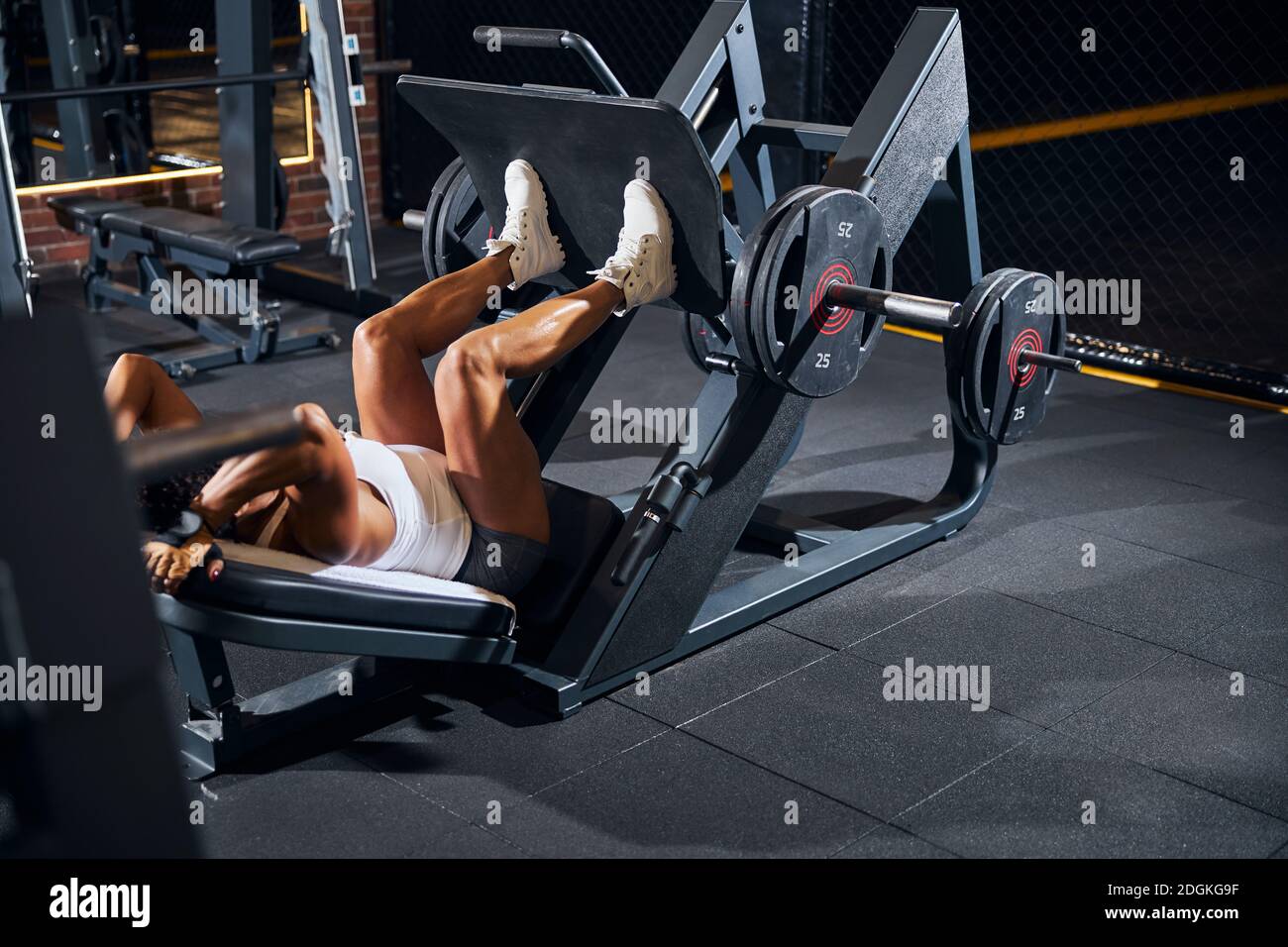 Sportswoman con testa riccia che fa la pressa inclinata della gamba Foto Stock