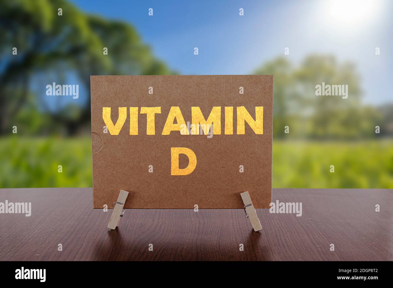 Testo della vitamina D sulla carta sul tavolo con sfondo verde soleggiato del parco. Foto Stock