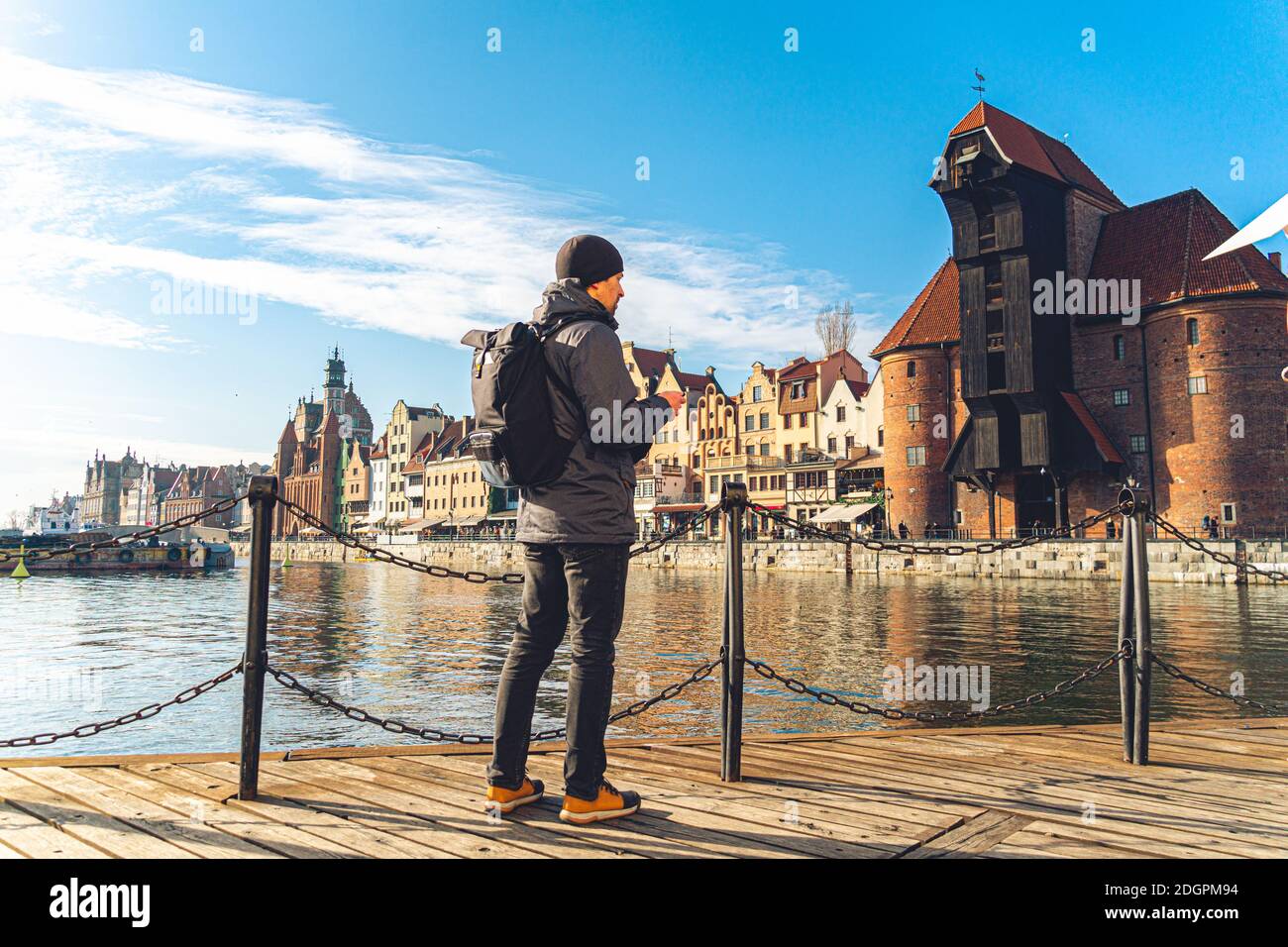 Tema del turismo in Polonia. Viaggiare a Danzica. Un viaggiatore maschile utilizza un telefono cellulare sull'argine del fiume Mottlawa in mezzo al ma Foto Stock