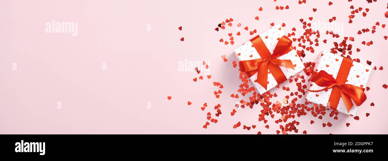 Scatole regalo bianche con fiocco di nastro rosso e confetti a forma di cuore rosso su sfondo rosa pastello. Banner San Valentino con regali. Madre giorno presente, b Foto Stock