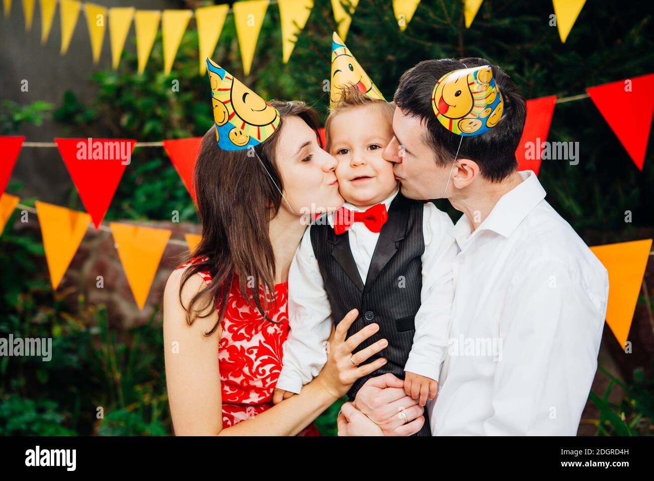 Festa di compleanno dei bambini. Il padre e la madre di famiglia tengono il figlio di un anno di nascita in armi e bacio cheekin sullo sfondo del parco Foto Stock
