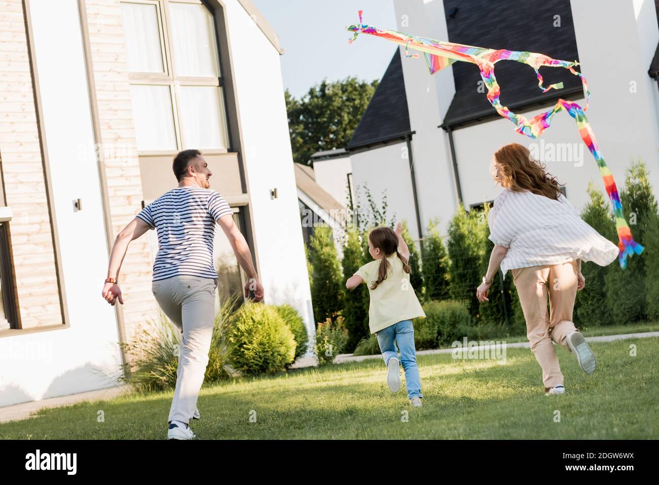 Vista posteriore della famiglia che corre mentre volando aquilone sul prato vicino a casa Foto Stock