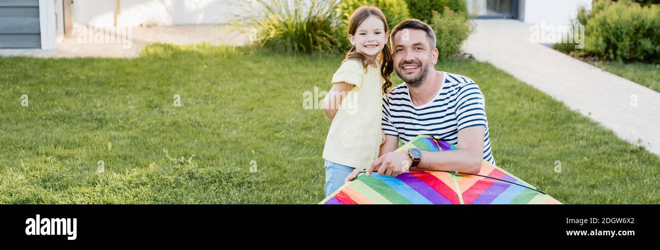 Felice figlia e padre con aquilone guardando la macchina fotografica sul prato, banner Foto Stock