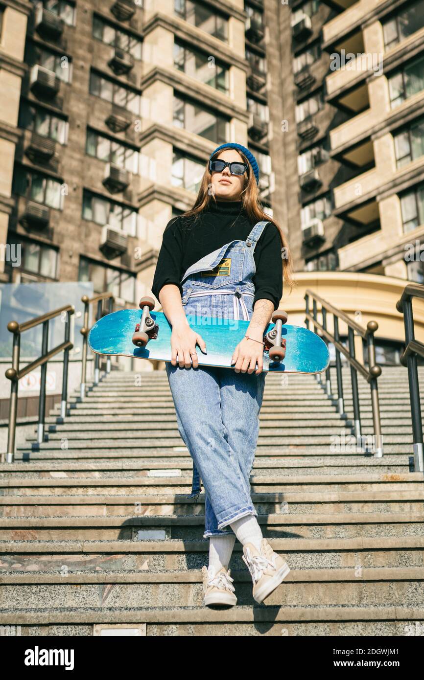Donna urbana con skate. Ragazza hipster con skateboard in città. Concetto di sport ed emozioni estreme. Stile di vita alternativo. Elegante Foto Stock