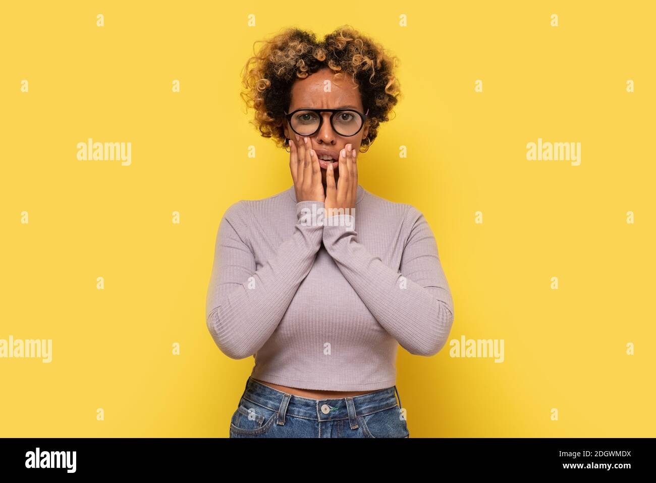 La giovane donna afro-americana pensierosa tiene il mento, sembra perplesso da parte, contempla qualcosa. Studio girato su parete gialla. Foto Stock
