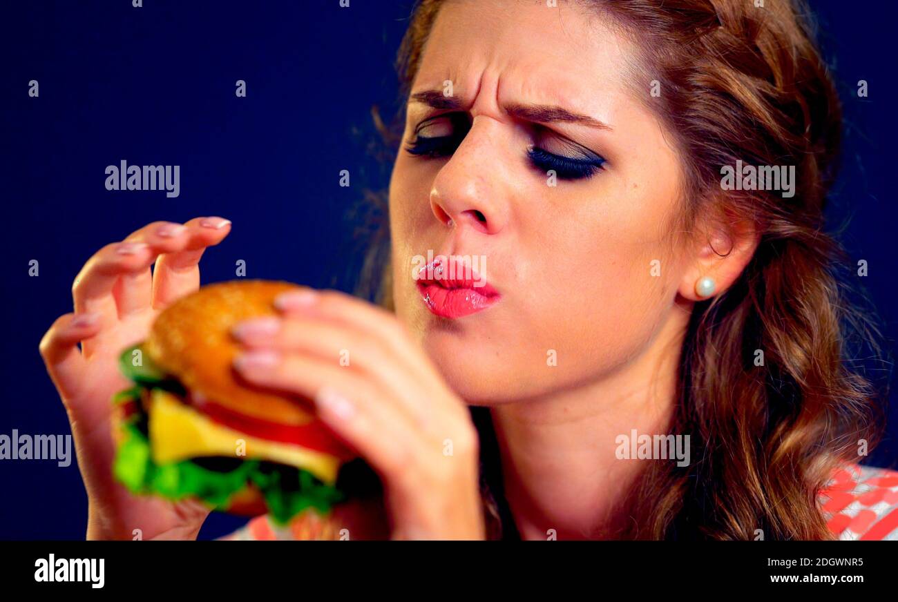 Donna che mangia hamburger. Faccia appetitosa della ragazza buon mangiare la spazzatura . Foto Stock