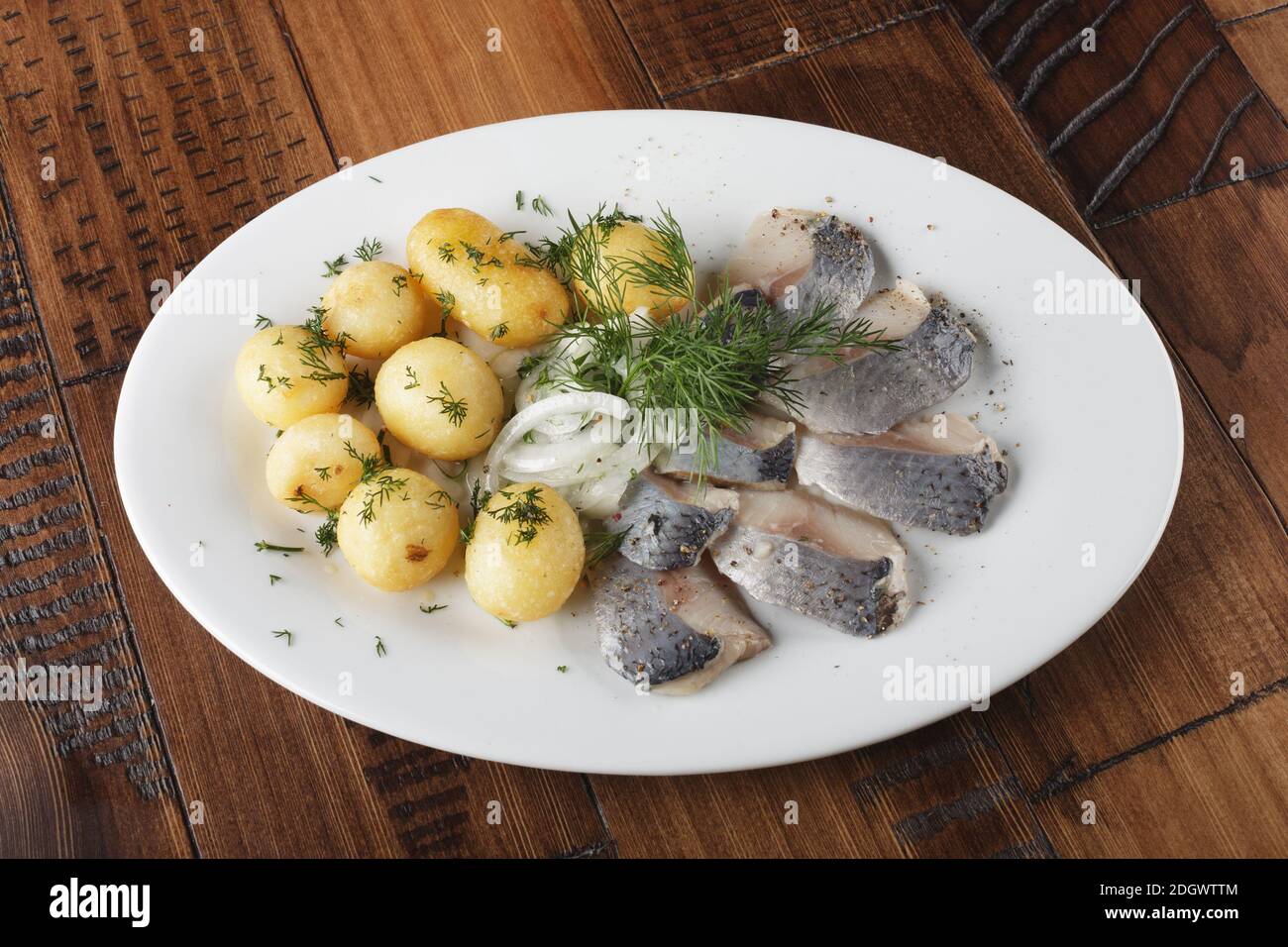 Pesce di aringa con palline di patate giovani su un piatto bianco. Sfondo di legno. Foto Stock