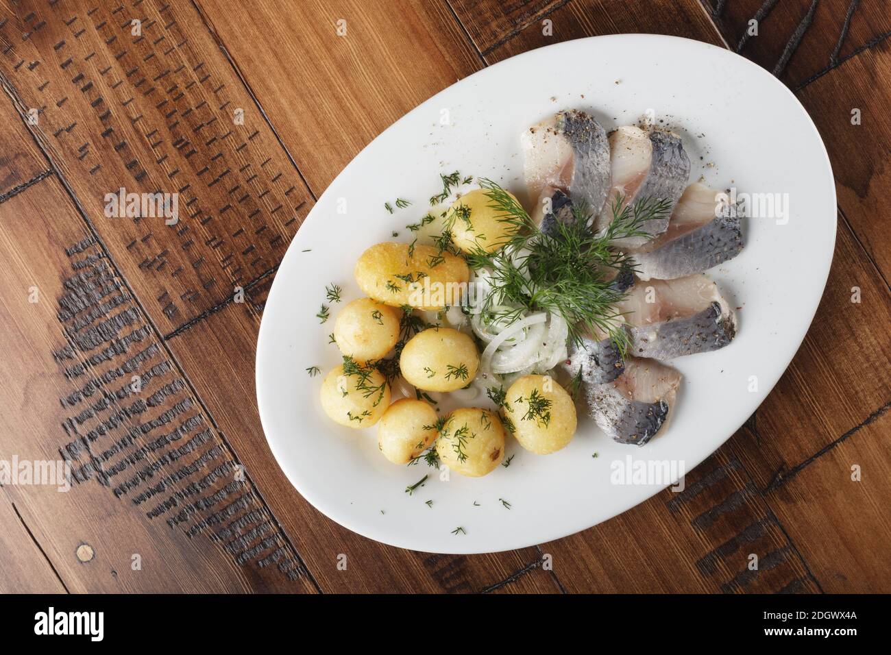 Pesce di aringa con palline di patate giovani su un piatto bianco. Sfondo di legno. Foto Stock