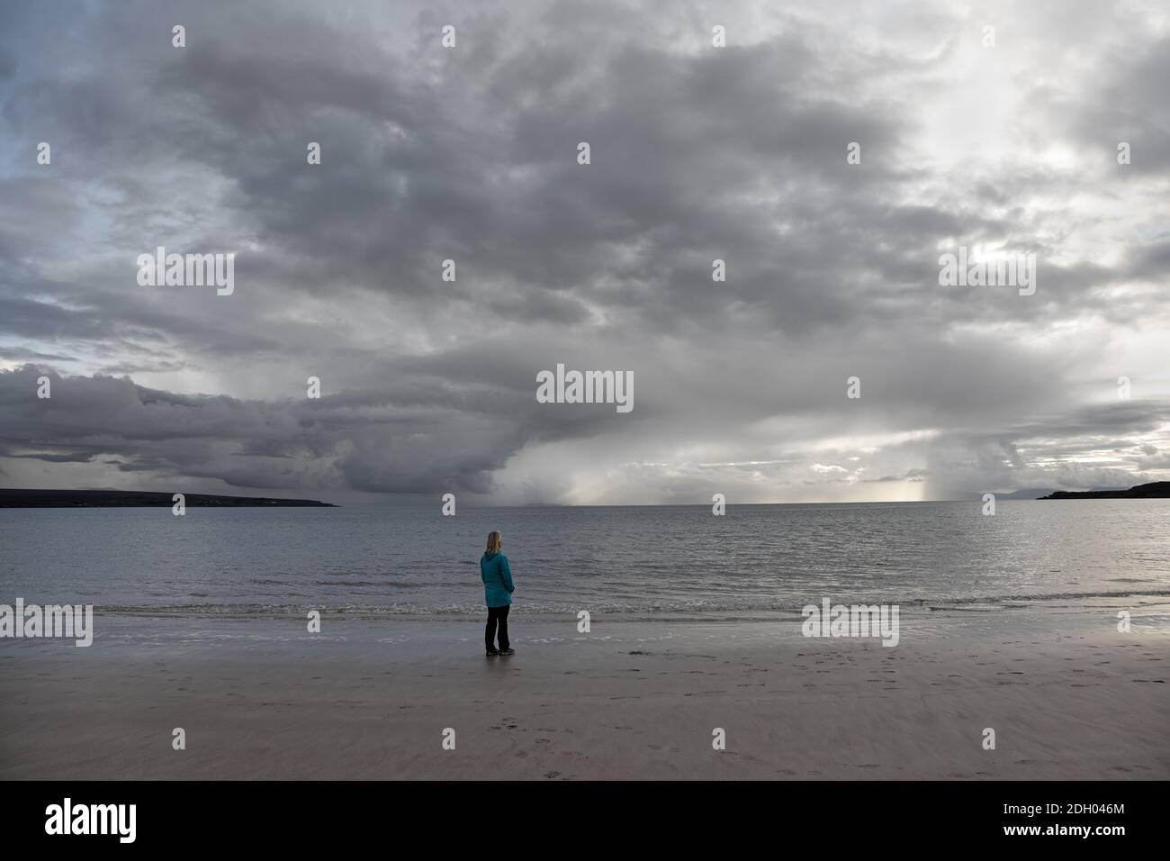 Donna su una spiaggia deserta che guarda verso le nuvole di tempesta Clearing sull'orizzonte, Sands Bay, Gairloch, Scozia, Regno Unito Foto Stock