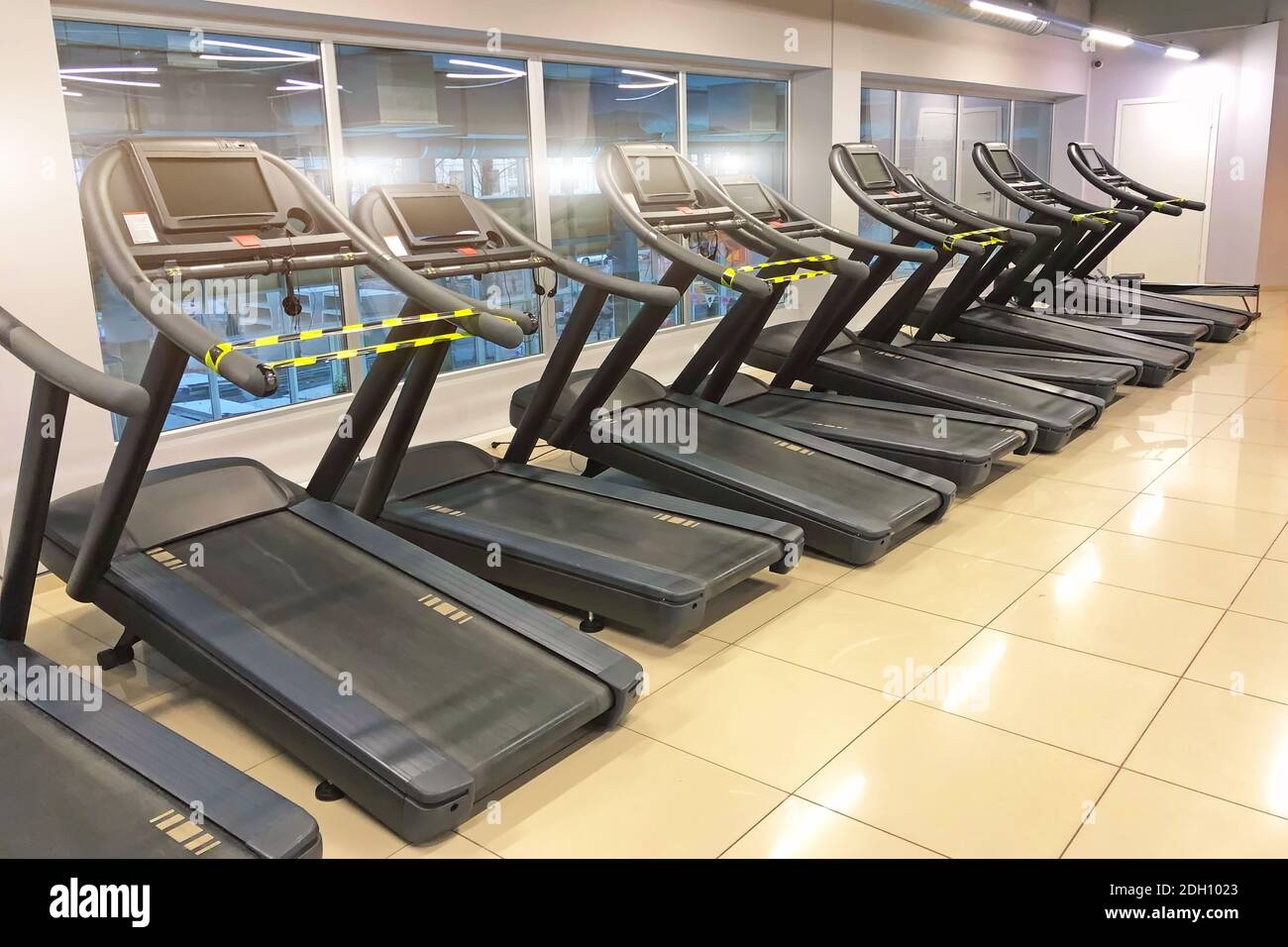 Tapis roulant chiusi con nastro segnaletico, separati da una distanza di sicurezza di 1.5-2 metri, per mantenere la distanza sociale nella zona cardio della palestra Foto Stock