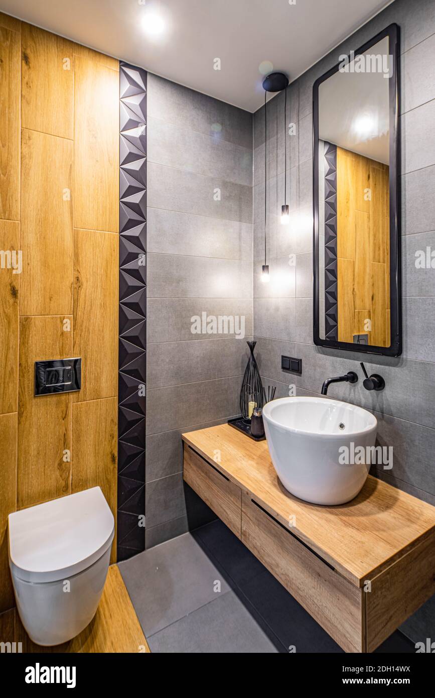 Interni contemporanei del bagno. Lavandino bianco e wc. Design in legno. Tessera grigia e nera. Foto Stock