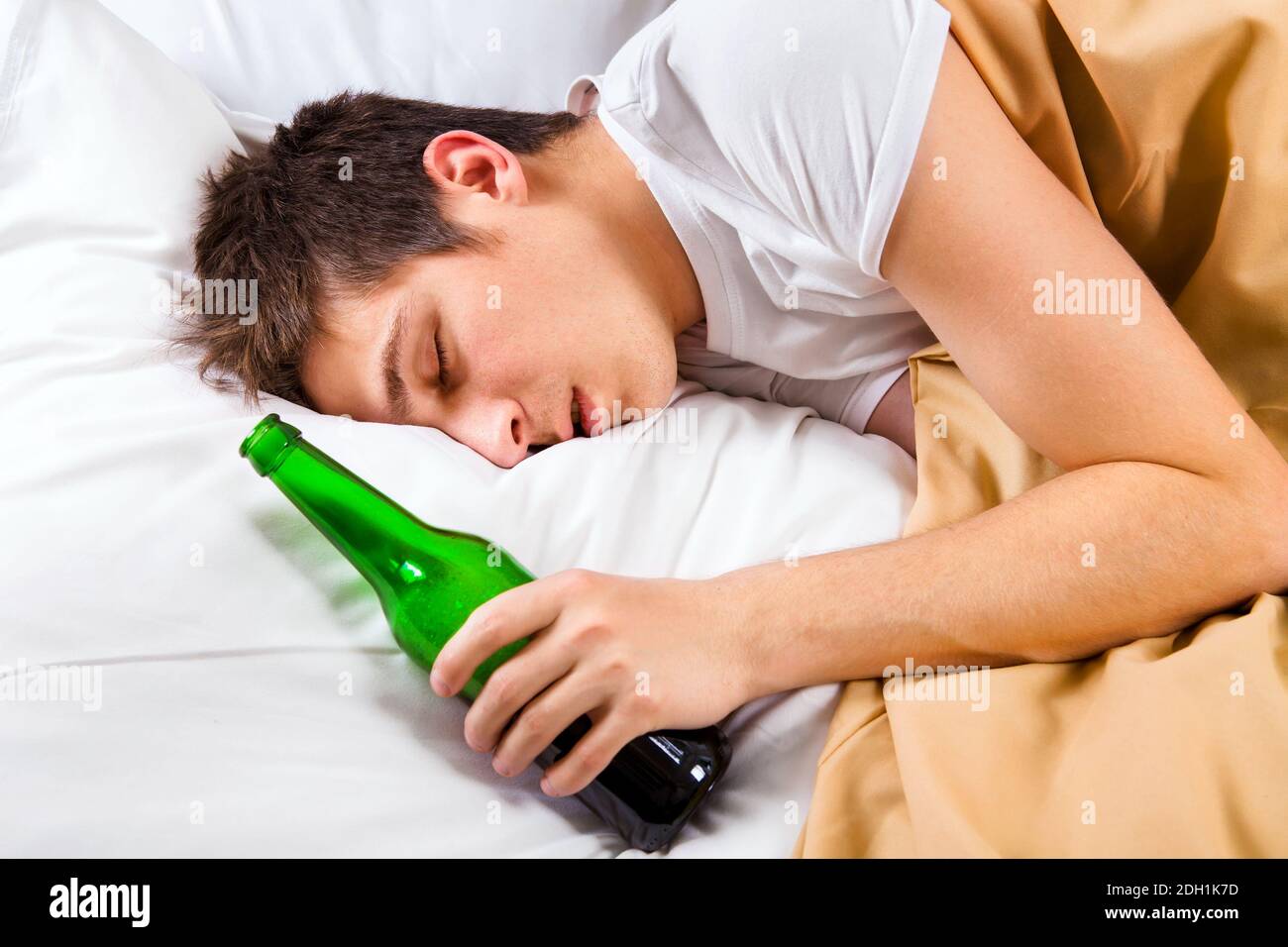 Il giovane uomo dorme con una bottiglia di birra nel letto A casa Foto Stock