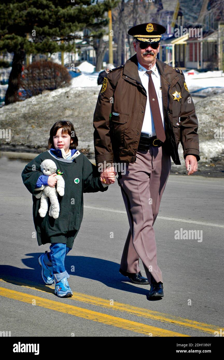 il poliziotto in uniforme cammina il bambino attraverso una strada trafficata Foto Stock