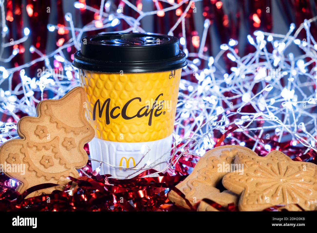 Primo piano di una tazza McCafe di colore giallo con pan di zenzero di forme diverse su sfondo festivo di Capodanno. Tinsel rosso e ghirlanda sullo sfondo. Kiev, Foto Stock