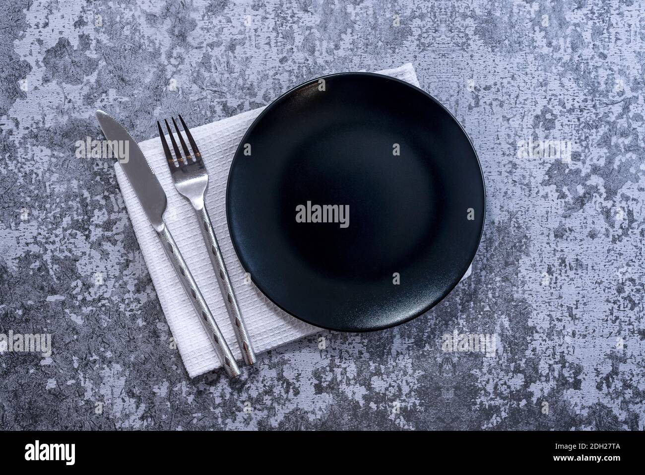 Piatto nero, posate con utensili e tovaglioli su rustico tavolo in pietra vista dall'alto. Impostazione del tavolo. Foto Stock
