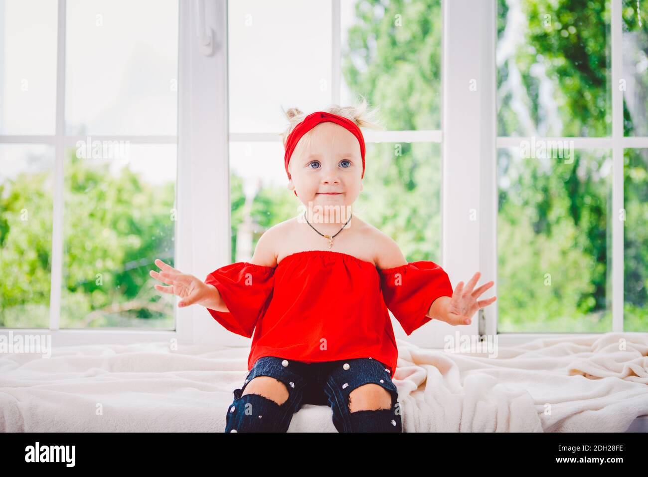 Bambina piccola divertente di due anni in eleganti vestiti rossi e jeans e  sneakers sul davanzale vicino alla finestra. Con un sorriso su h Foto stock  - Alamy