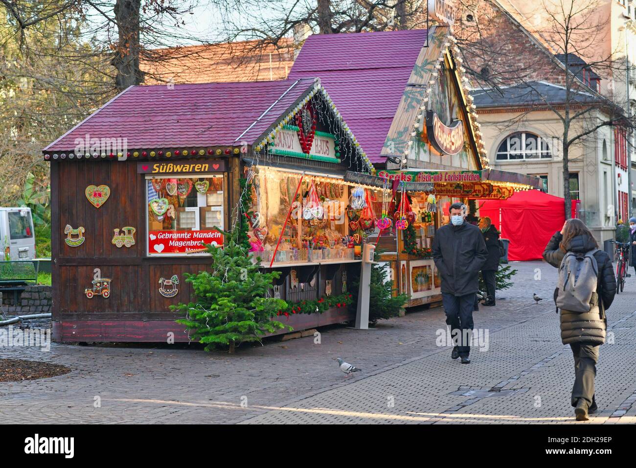 Heidelberg, Germania - Dicembre 2020: Festa decorato mercatino di Natale vendita stand vendita di cibo e bevande con la gente in maschere a piedi Foto Stock