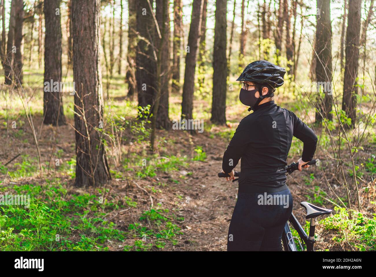 Donna sportiva attiva in mountain bike su sentiero forestale, indossando una maschera viso contro l'inquinamento atmosferico e covid19 coronavirus. CITR Foto Stock