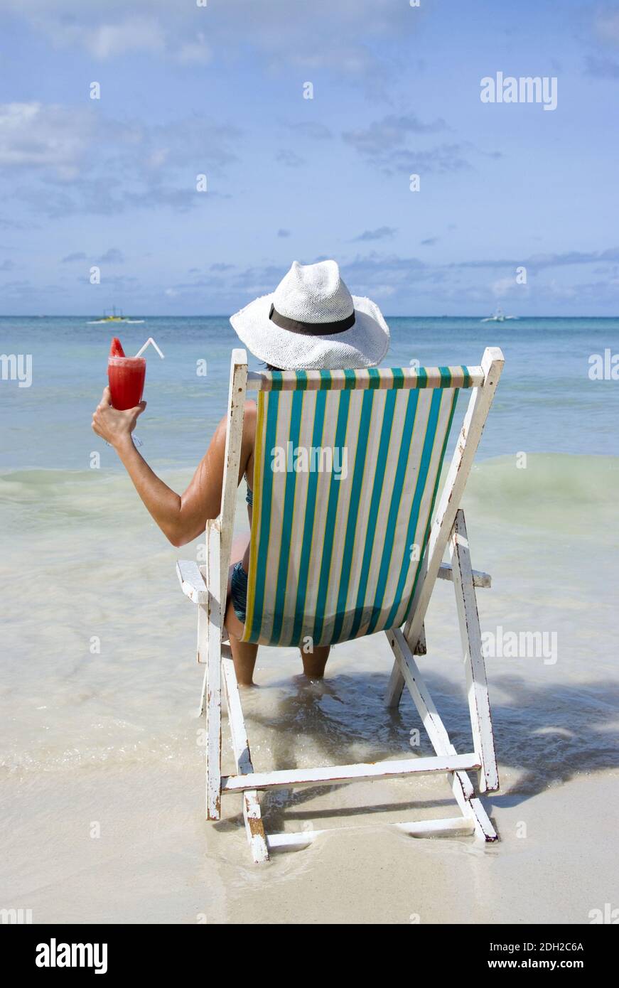 Frau auf Soinnenstuhl sitzt am Strand und geniesst einen Cocktail, Philippinen, Insel Boracay, signor: Sì Foto Stock