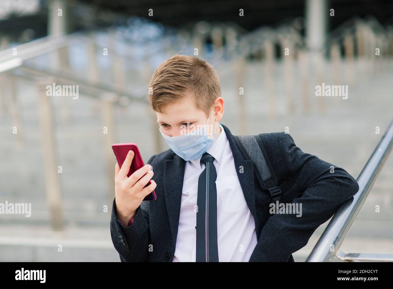 Scolaro esce dalla scuola indossando una maschera protettiva nel città Foto Stock