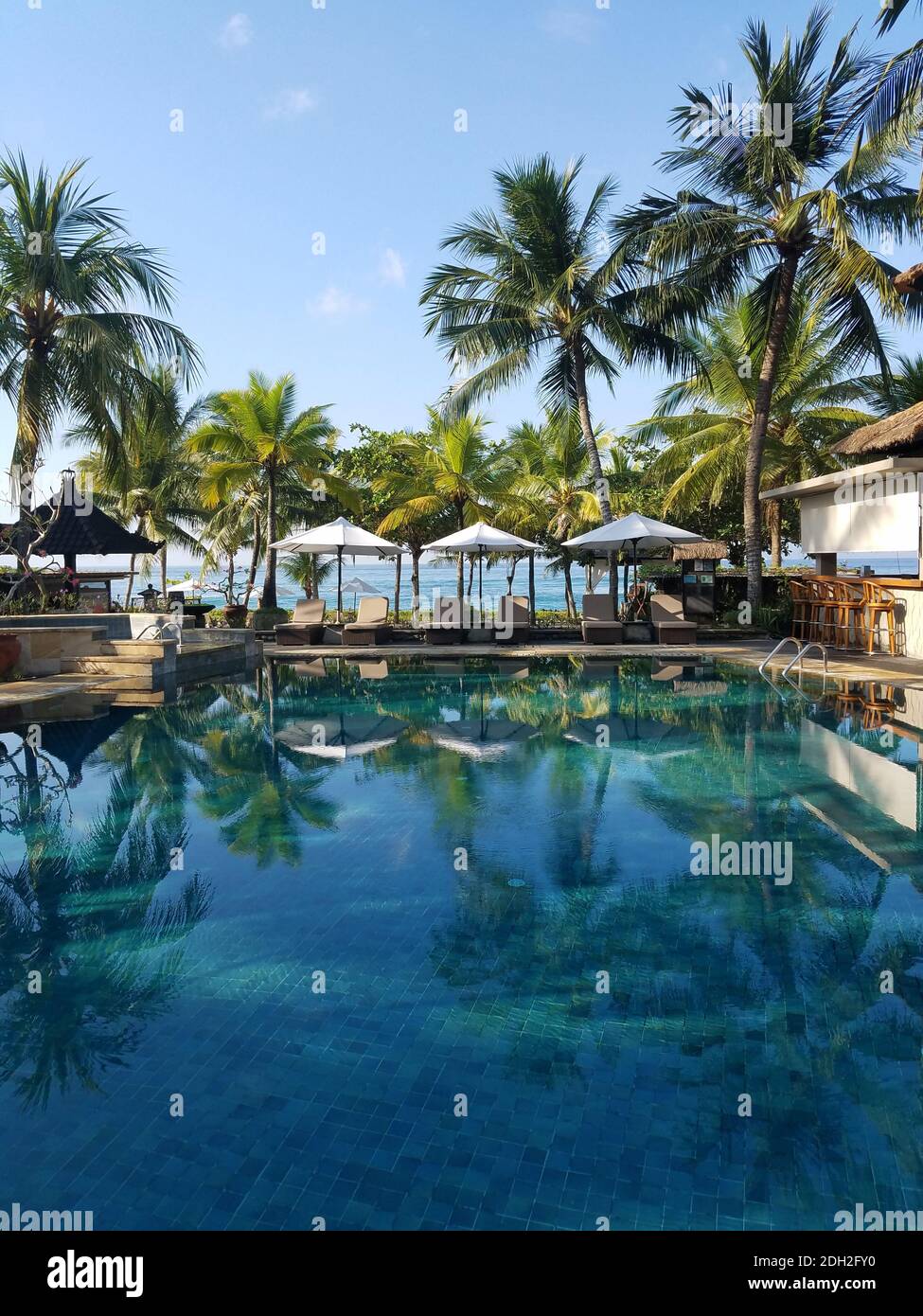 Piscina e bar circondati da palme, in un resort sulla spiaggia di Candidasa a Bali, Indonesia, per viaggi di background. Foto Stock