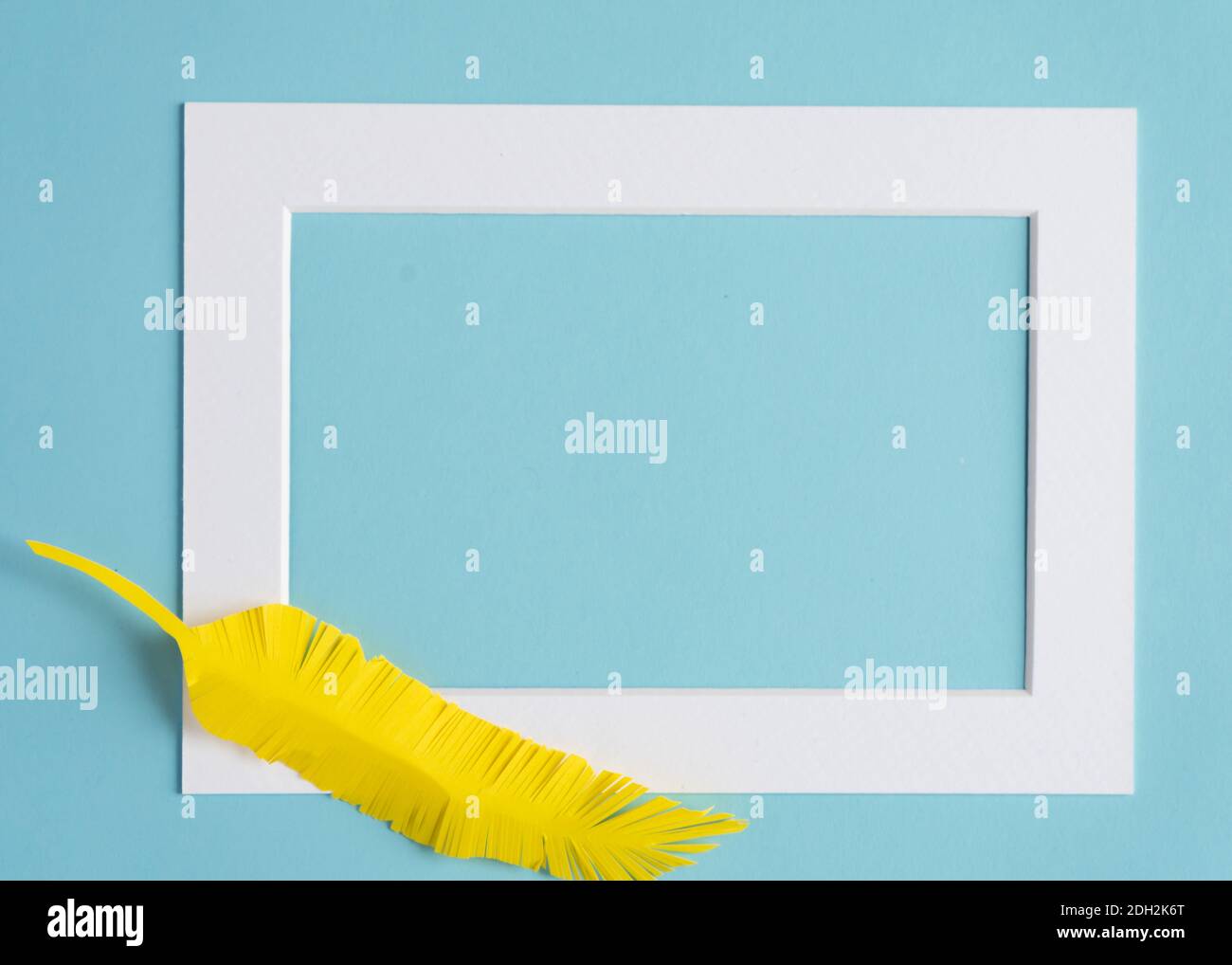 cornice bianca con piuma di carta gialla su sfondo colorato con spazio di copia Foto Stock