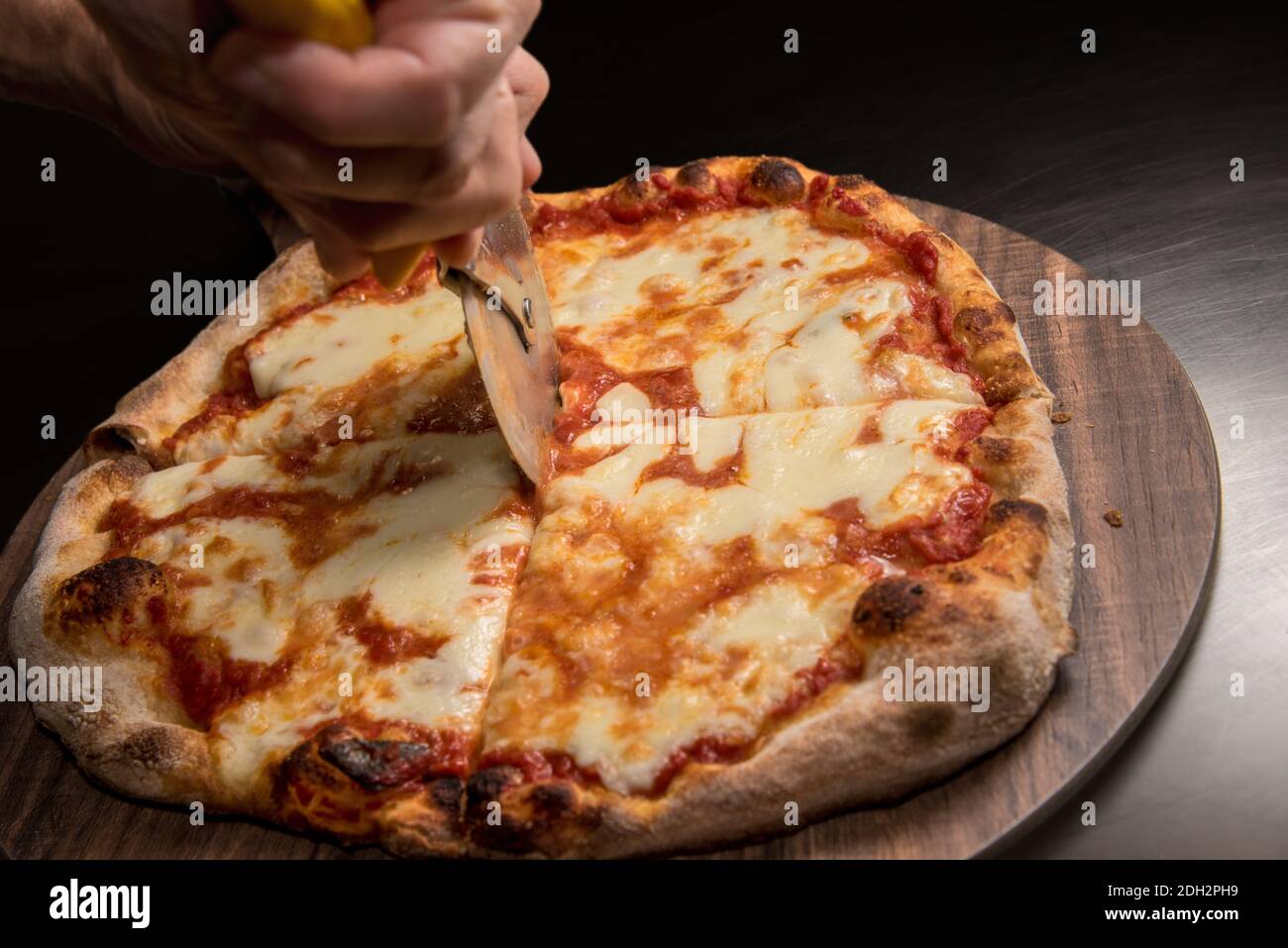 pizza con salsa di pomodoro e mozzarella, mano dello chef con fette di coltello a rullo su tagliere di legno Foto Stock