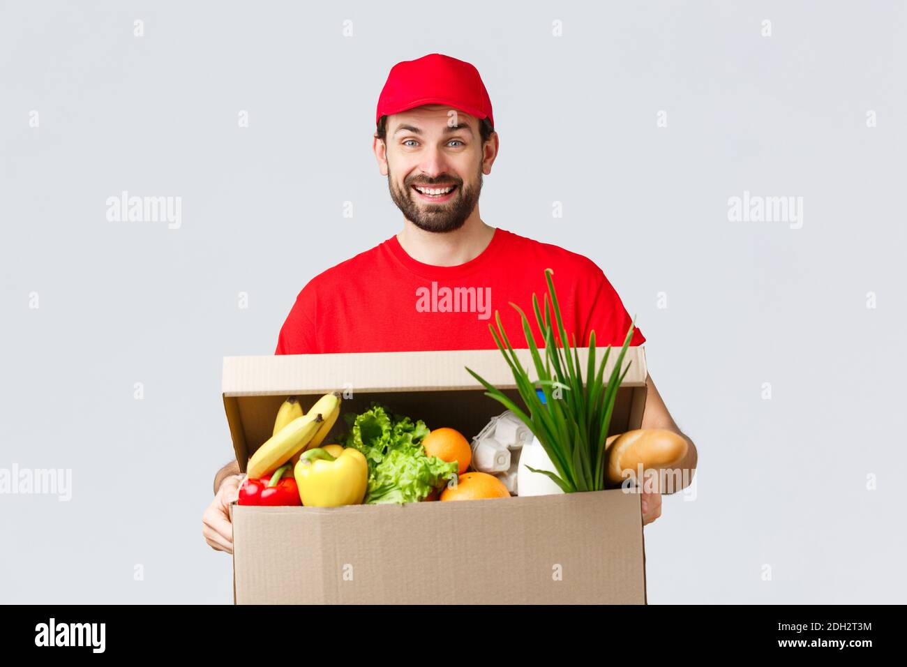 Generi alimentari e consegna pacchi, covid-19, quarantena e concetto di shopping. Sorridente delivery man in uniforme rossa, portare cliente o. Foto Stock