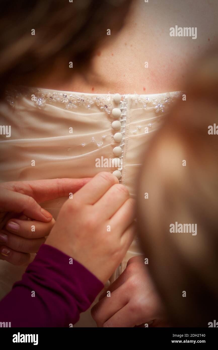 Bridesmaid sta allacciando abito da sposa bianco per la sposa. Foto Stock