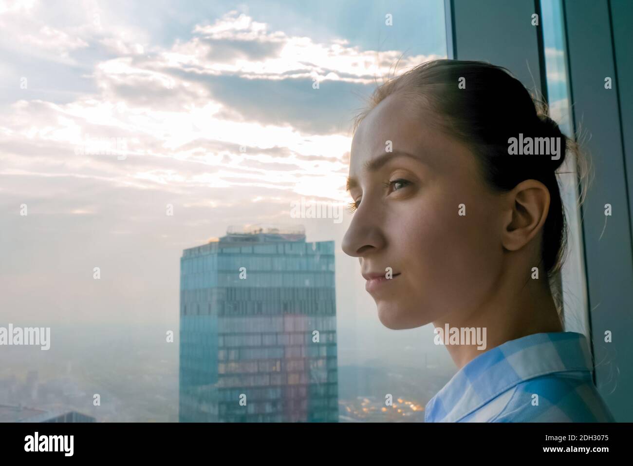 Ritratto di donna che guarda il paesaggio urbano attraverso la finestra del grattacielo - primo piano Foto Stock