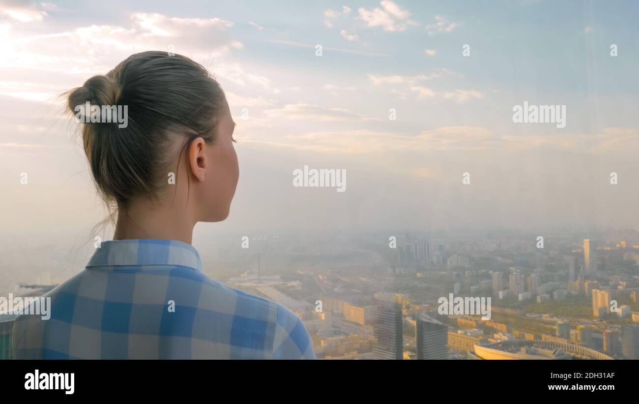 Donna che guarda il paesaggio urbano attraverso la finestra del grattacielo - indietro visualizza Foto Stock