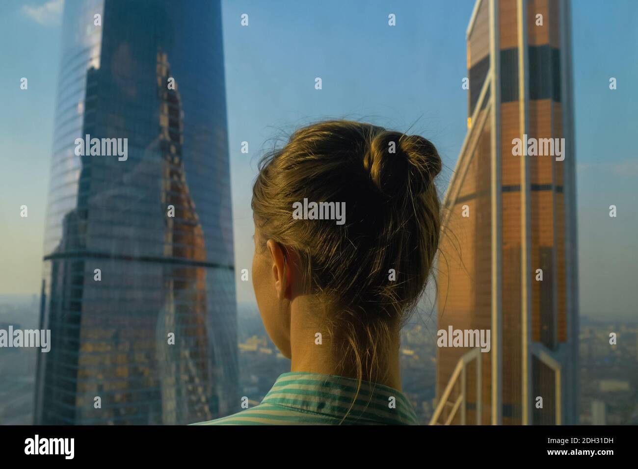 Vista posteriore di donna che guarda il paesaggio urbano attraverso la finestra di grattacielo Foto Stock
