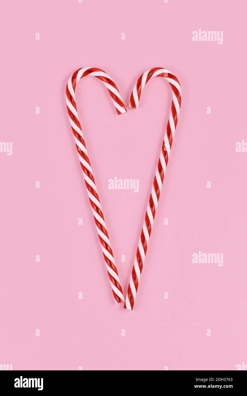 Canne di caramelle di Natale che formano la forma del cuore su sfondo rosa Foto Stock
